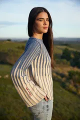 Sweater de punto con diseño de rayas verticales en relieve, combinando colores azul y crudo. Presenta mangas largas acampanadas con un detalle bordado en color rojo en la parte inferior.