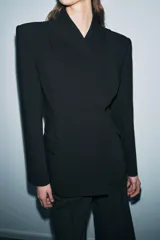 Blazer entallada de Zara Woman Collection, color negro, con escote en pico, manga larga con hombreras y cierre frontal con botones ocultos. Presenta bolsillos con solapa en el delantero y detalle de nervios marcados.
