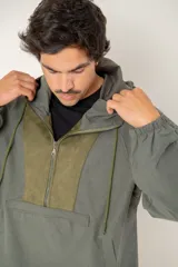 Canguro tipo anorak de color verde militar, con capucha ajustable y cierre frontal parcial. Presenta un panel central en contraste de textura gamuzada y un bolsillo frontal tipo canguro con solapa.