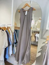 Vestido largo sin mangas, color beige claro, con escote en V y textura arrugada o arrugada, con terminación deshilachada en el ruedo.