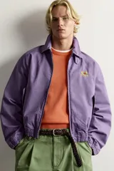 Cazadora regular fit de algodón color violeta con efecto lavado, cuello solapa y cierre de cremallera de doble dirección. Posee bordado frontal de gráficos Fruit of the Loom, bolsillos de vivo en la cadera y acabados con elástico.
