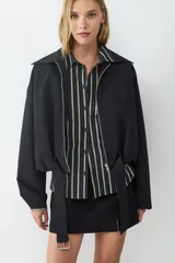 Campera corta de manga larga confeccionada en tejido técnico color negro. Presenta cuello solapa, cierre frontal con cremallera metálica y cinturón integrado con hebilla en la cintura.