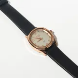 Reloj de pulsera con caja dorada de forma octogonal y esfera blanca con números arábigos. Correa de cuero negra.