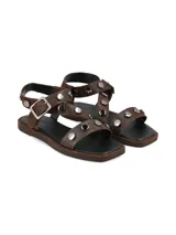 Sandalias planas de cuero marrón con tiras decoradas con tachas metálicas redondas y hebilla de ajuste lateral.