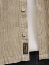 Sobrecamisa de manga larga confeccionada en pana, con cuello camisero, cierre frontal de botones, puños abotonados y un bolsillo en el pecho con etiqueta de marca. Presenta un corte relajado y textura acanalada.