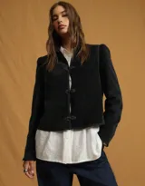 Chaqueta negra de estilo oriental con cuello alto estructurado y cierre frontal mediante nudos decorativos tradicionales. Presenta mangas largas con leve volumen en los hombros y un corte recto.