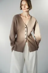 Saco ajustado de punto acanalado suave, con escote en V y botonadura frontal con cuatro botones oscuros. Modelo de cintura entallada con hombros ligeramente caídos y mangas largas con puños ceñidos.