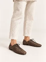 Zapato plano marrón de cuero vacuno con textura granulada, diseño acordonado de perfil bajo y suela fina.