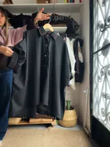 Camisa oversize de lino color negro, con cuello clásico, cierre frontal con botones y detalles de costuras bordadas en color rojo. Presenta mangas anchas y corte holgado.