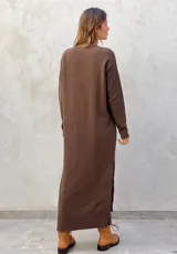 Vestido midi de punto color azul marino, con cuello en V, mangas largas y diseño holgado. Presenta un patrón de rombos en relieve y aberturas laterales con botones decorativos en el ruedo.