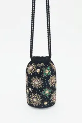 Cartera tipo bolso de mano color negro, confeccionada en terciopelo con bordados de estrellas y aplicaciones de pedrería brillante. Cuenta con correas trenzadas de cordón negro y cierre superior.