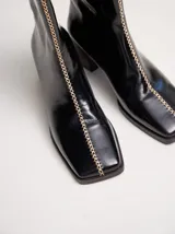 Botas de cuero negro con punta cuadrada, taco ancho de madera y costura decorativa bordada en contraste a lo largo del empeine. Cuenta con cierre en la parte trasera.