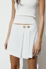 Falda pantalón de tiro bajo con diseño de pliegues en el delantero y cierre frontal con botones metálicos decorativos.