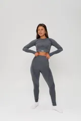 Conjunto deportivo de dos piezas compuesto por un top de manga larga tipo crop top con aberturas para pulgares y una calza de tiro alto. Ambas prendas presentan un diseño seamless con detalles de texturas perforadas y el logo de la marca estampado en el frente.