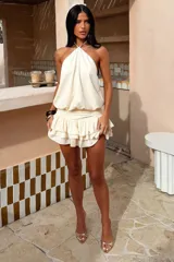 Vestido corto color beige, con escote halter, espalda descubierta y falda con volados en capas.