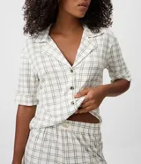Pijama corto de dos piezas confeccionado en viscolycra con estampado de cuadros. Compuesto por una camisa de mangas cortas con cuello de solapa y cierre frontal de botones, y un short con cintura elastizada.