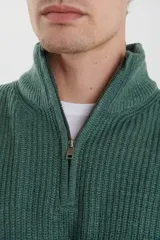 Sweater verde de punto inglés con cuello alto y cierre metálico frontal. Tiene mangas largas y terminaciones en punto canalé.