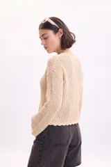 Sweater de punto fantasía con lurex en color beige, cuello redondo y mangas largas con terminaciones en ondas.