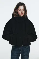 Chaqueta acolchada de corte corto con cuello subido y capucha. Presenta cierre frontal con cremallera termosellada y solapa con botones a presión, bolsillos laterales con cierre, mangas largas con puños elásticos y bajo ajustable con cordones.