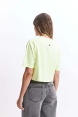 Remera corta (cropped) de algodón color verde lima, con cuello redondo y manga corta. Presenta un pequeño estampado en el pecho con un corazón naranja y texto manuscrito.