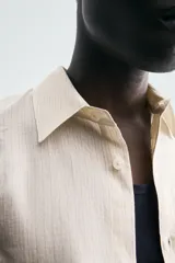 Camisa de hombre de corte relajado (relaxed fit) en tejido de mezcla de algodón y viscosa, color beige claro con finas rayas verticales. Presenta cuello italiano y manga larga con puño abotonado.