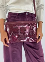 Cartera tipo sobre con lentejuelas doradas y negras reversibles, con borde superior de cuero negro y correa fina de cuero negro.