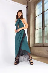 Vestido largo verde petróleo de seda lavada, con escote halter cruzado, abertura en el abdomen, falda con capas y flecos.