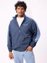 Campera rompevientos Rusty de nylon, color azul con detalles en azul claro en las mangas. Presenta cierre frontal, cuello alto y puños elásticos.