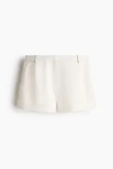 Short de sastre de tiro alto, color beige, con bolsillos al bies y pinzas moldeadoras. Cierre frontal con cremallera y corchete oculto.