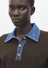 Chaleco de punto color marrón, con cuello polo y cierre frontal parcial con botones dorados, y detalles en denim en la zona del cuello.