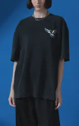 Remera de manga corta con cuello redondo y calce oversize, confeccionada en algodón premium con efecto de lavado nevado. Presenta una estampa gráfica en la espalda con diseño de palomas y texto alusivo.