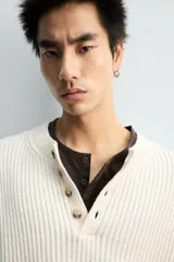 Jersey de punto acanalado en color crudo, con cuello redondo y cierre frontal de botonadura tipo panadero. Presenta manga larga y acabados en rib.