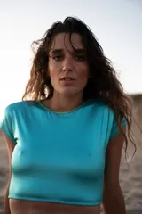 Conjunto de bikini compuesto por un top corto de manga corta y espalda abierta, y una bombacha tipo vedetina. Ambas piezas están confeccionadas en lycra brillante de color turquesa con detalles en verde lima.