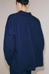 Camisa de corte oversize confeccionada en mezcla de viscosa con textura de rayas verticales en jacquard. Presenta cuello solapa, cierre frontal con botones, bolsillo de plastrón en el pecho, mangas largas con puños anchos y bajo redondeado.