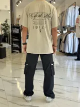 Remera oversize color beige, con mangas corta y gran estampado gráfico en la espalda con texto en negro.