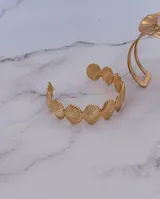 Brazalete abierto de acero dorado, compuesto por dijes con forma de conchas marinas unidas entre sí.