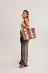 Cartera grande de cuero color marrón con asas de cuero con estampado animal print y ojales dorados.