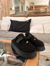 Suecos de símil gamuza color beige, con interior forrado en corderito sintético, plataforma y detalle de tira frontal con cordones y punteras metálicas.