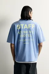 Camiseta relaxed fit de color celeste con efecto acid wash, cuello redondo y manga corta. Cuenta con estampa frontal con la inscripción "HOTEL STAFF" y "Escape Ibiza" en tonos amarillos.
