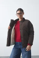 Campera acolchada de nylon color negro, con cuello alto, cierre frontal y botones a presión. Presenta un diseño de rombos y forro interior suave.