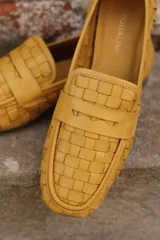 Mocasines de cuero napa color mostaza, con diseño entrelazado, corte clásico y detalle de antifaz en el empeine.