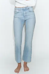 Jeans de tiro alto con diseño cropped flare, confeccionados en denim azul con acabado desgastado. Presentan cinco bolsillos, cierre frontal con cremallera y botón metálico, y bajo con terminación sin costuras.