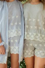 Conjunto de pijama compuesto por una musculosa de escote redondo y un short con elástico en la cintura. Ambas piezas están confeccionadas en tela a rayas finas con detalles bordados florales y terminaciones con puntilla festoneada.