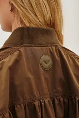 Campera bomber de corte holgado en color marrón, con cuello, puños y ruedo de tejido elástico acanalado. Presenta cierre frontal y diseño de mangas con volumen.