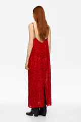 Vestido midi de corte recto con escote en V, tirantes dobles finos y cierre frontal con botones. Presenta un diseño estampado con manchas oscuras sobre fondo rojo.