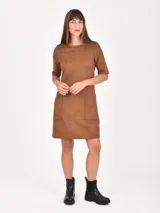 Vestido corto de corte recto y estilo minimalista, confeccionado en tela tipo gamuza negra. Presenta cuello redondo, mangas cortas y dos bolsillos frontales aplicados a la altura de la cadera.