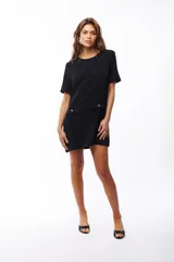 Vestido corto negro de poliéster y elastano, con cuello redondo y mangas cortas. Presenta dos bolsillos frontales con botón dorado.