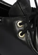 Zapato tipo Oxford de cuero negro con cordones, ojales metálicos dorados y taco ancho.