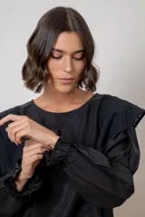 Blusa blanca de algodón con cuello redondo, mangas largas con puños elásticos y volados decorativos en los hombros.