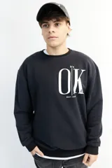 Buzo negro de corte oversize con cuello redondo y puños ajustados. Estampa frontal con la frase "It's OK" en letras blancas.